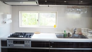 A modern kitchen with a gas stove, built-in dishwasher, and a window with a view of greenery. - Condominium Orchid House Nakijin (Nakijin)