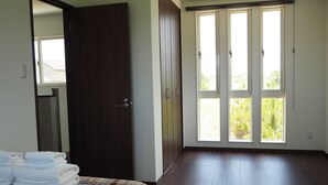 A bedroom with a bed, a door, and a large window with a view of greenery. - Condominium Orchid House Nakijin (Nakijin)
