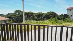 A wooden deck with a metal railing overlooking a road and greenery. - Condominium Orchid House Nakijin (Nakijin)