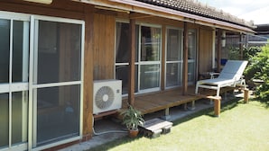 Ett trähus med ett tak täckt av takpannor, stora fönster, en träveranda och en solstol.