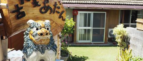 A ceramic lion statue in front of a house with a tiled roof and a large wooden sign with Japanese characters.