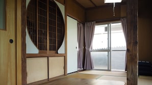 Ett traditionellt japanskt rum med tatamimattor på golvet, en skjutdörr och ett stort fönster med gardiner.