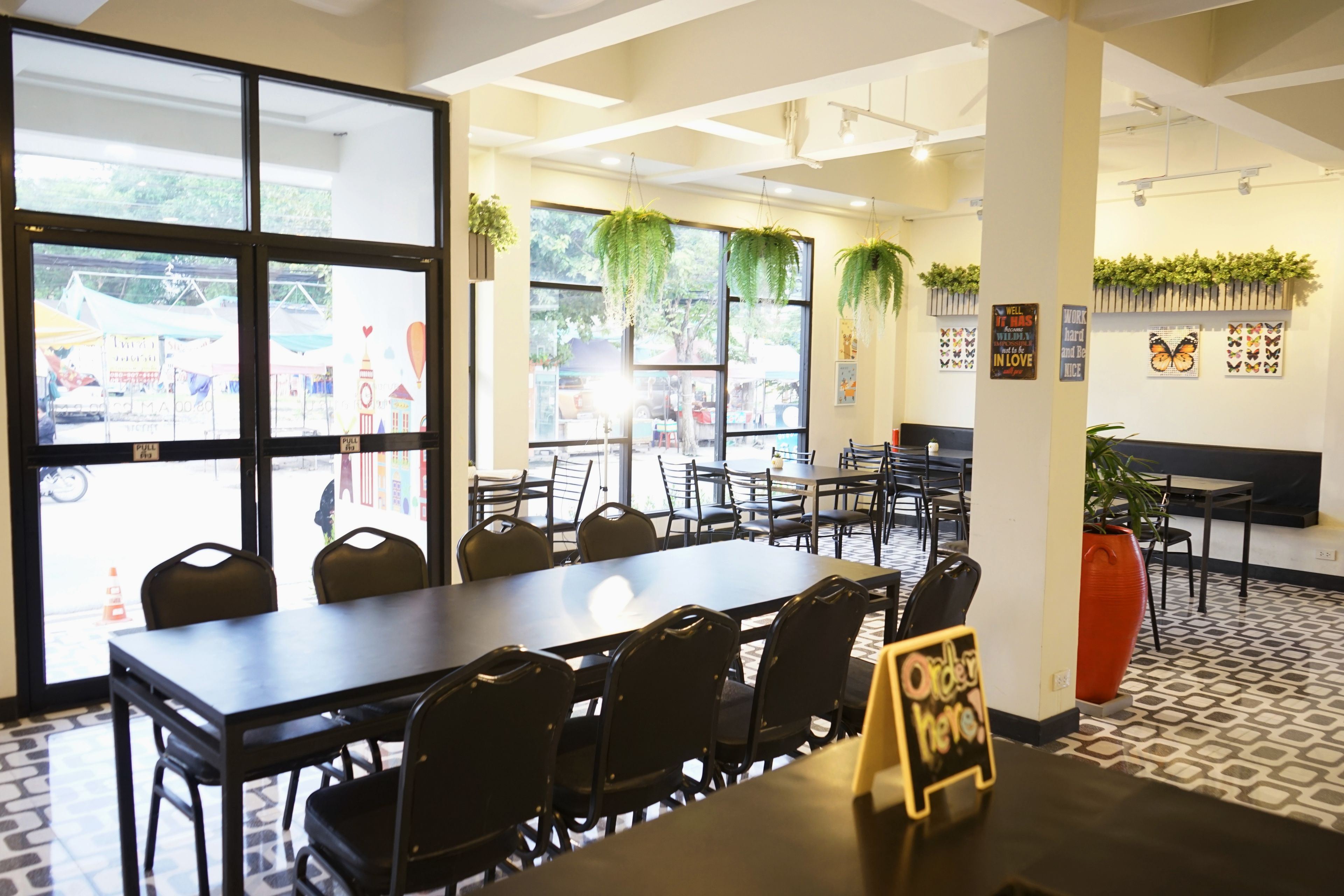 A spacious indoor area with multiple tables and chairs, large windows with views of the outside, and decorative plants.