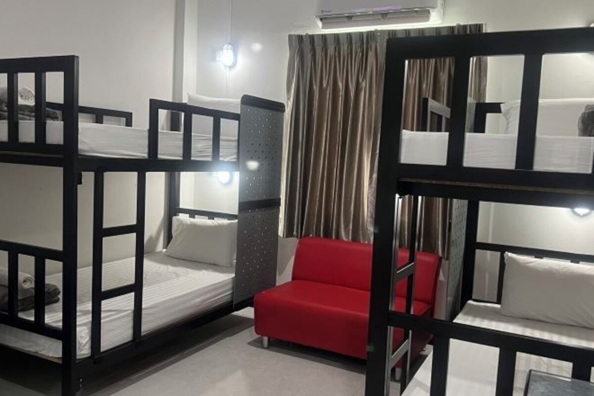 Um quarto com beliches, uma cadeira vermelha e uma cortina.
