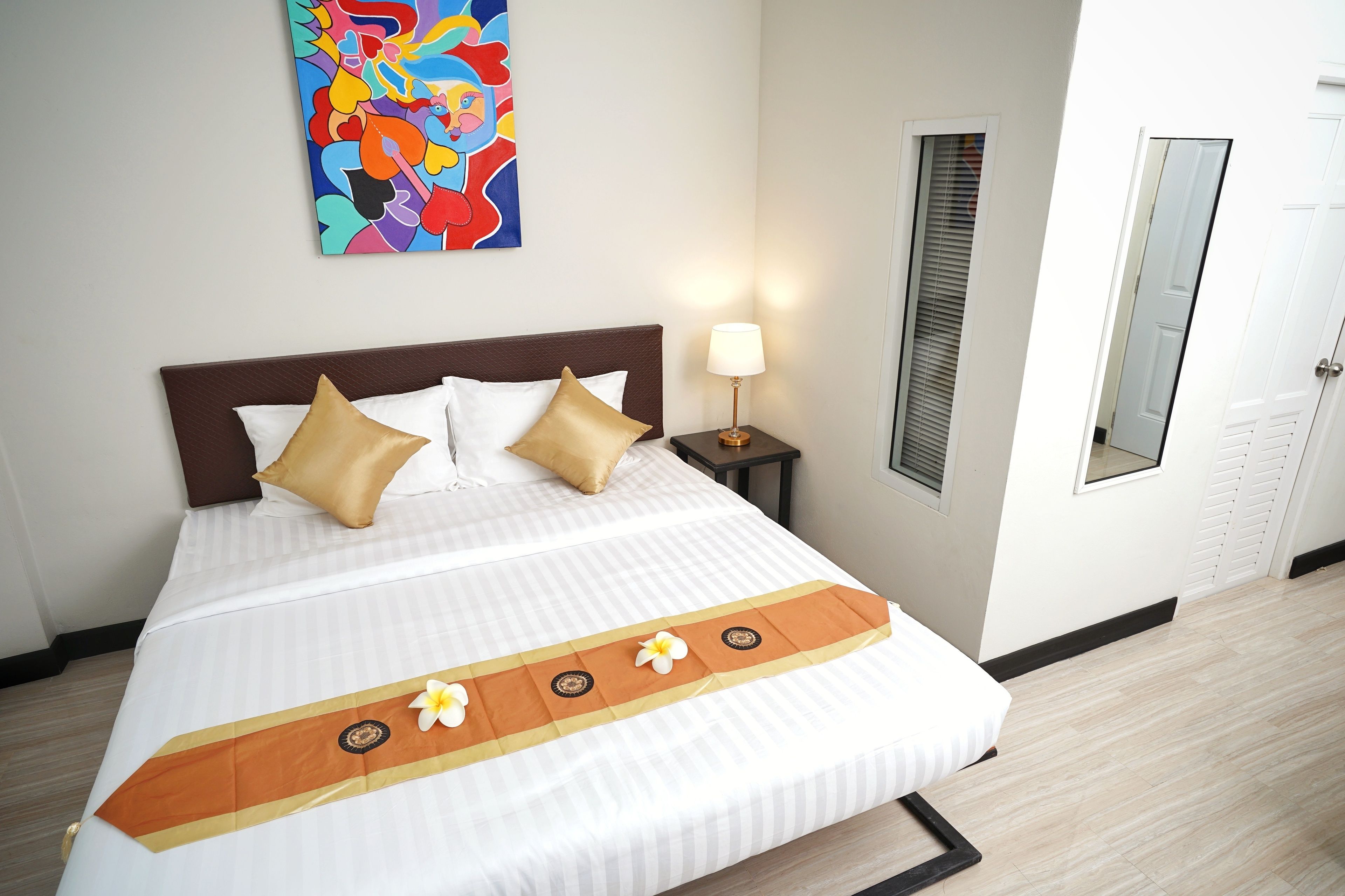 Una cama bien hecha con una colcha a rayas, dos almohadas y un cabecero decorativo anaranjado y blanco.