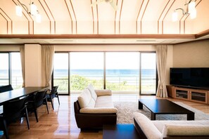A spacious living room with a large sofa, a dining table, and a flat-screen TV. - Private villa LUXE (Nakijin)