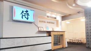 Zona de recepción de un hotel con un letrero que dice 'Hotel Samuraiai' y una pantalla digital con caracteres japoneses.