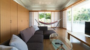 A modern living room with a sofa, a glass coffee table, a hammock, and a TV. - N.C.Kouri (Nakijin)