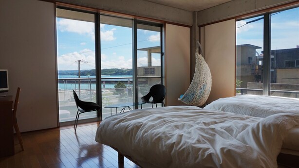A bedroom with a large window, a hammock, and a view of a body of water. - N.C.Kouri (Nakijin)