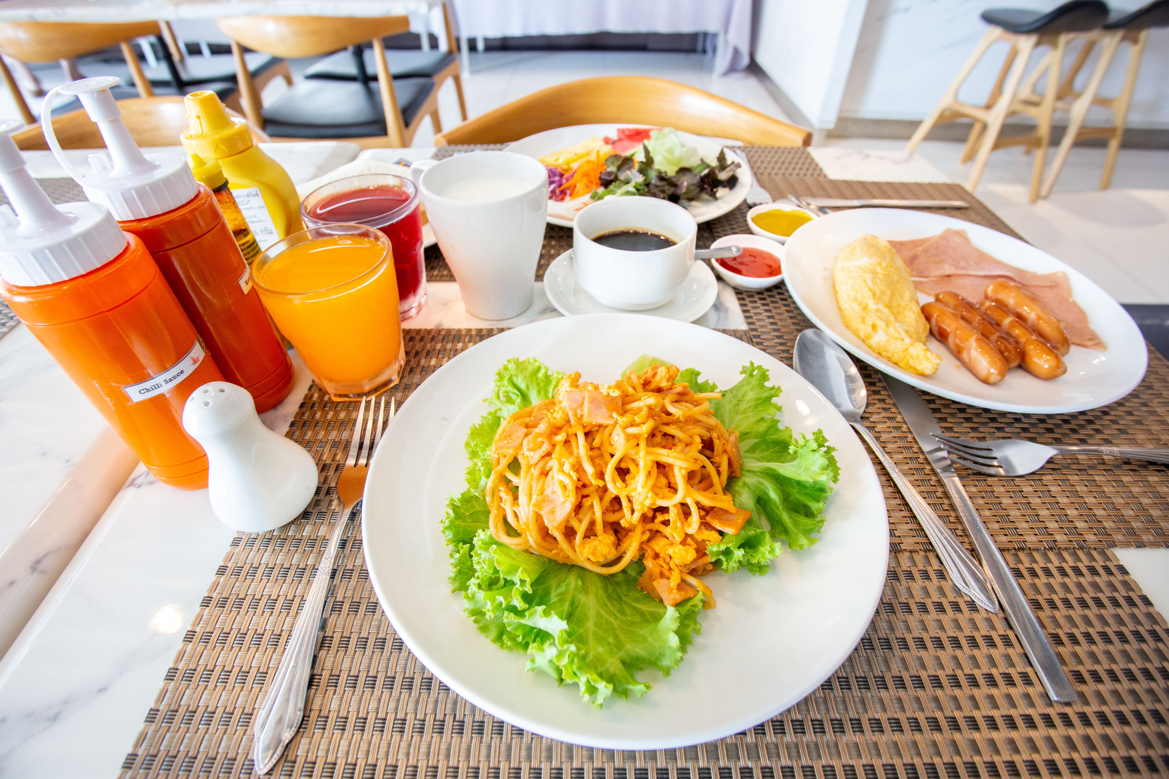 A breakfast table with a plate of noodles, a cup of coffee, and various condiments.