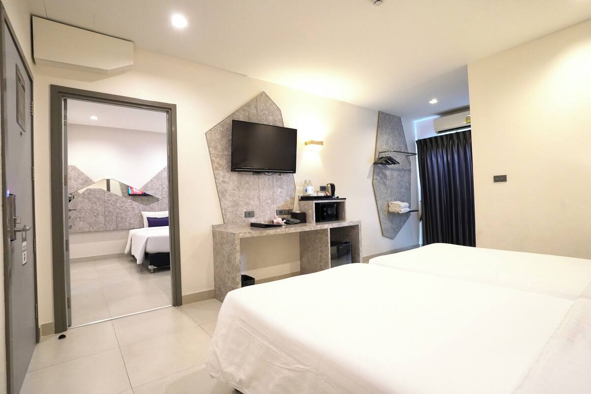 A modern hotel room with a large bed, a flat-screen TV mounted on the wall, a desk with a chair, and a mirror.