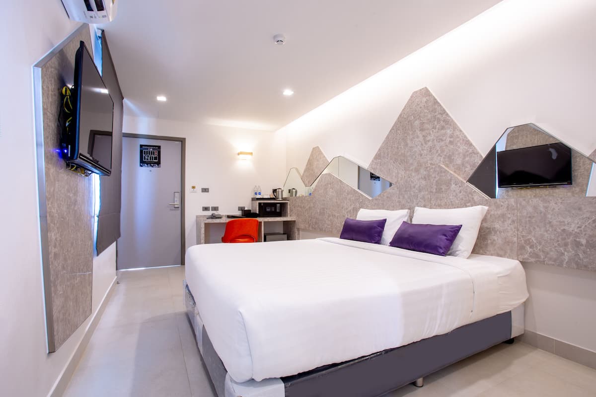 A modern hotel room with a large bed, a desk, and a TV mounted on the wall.