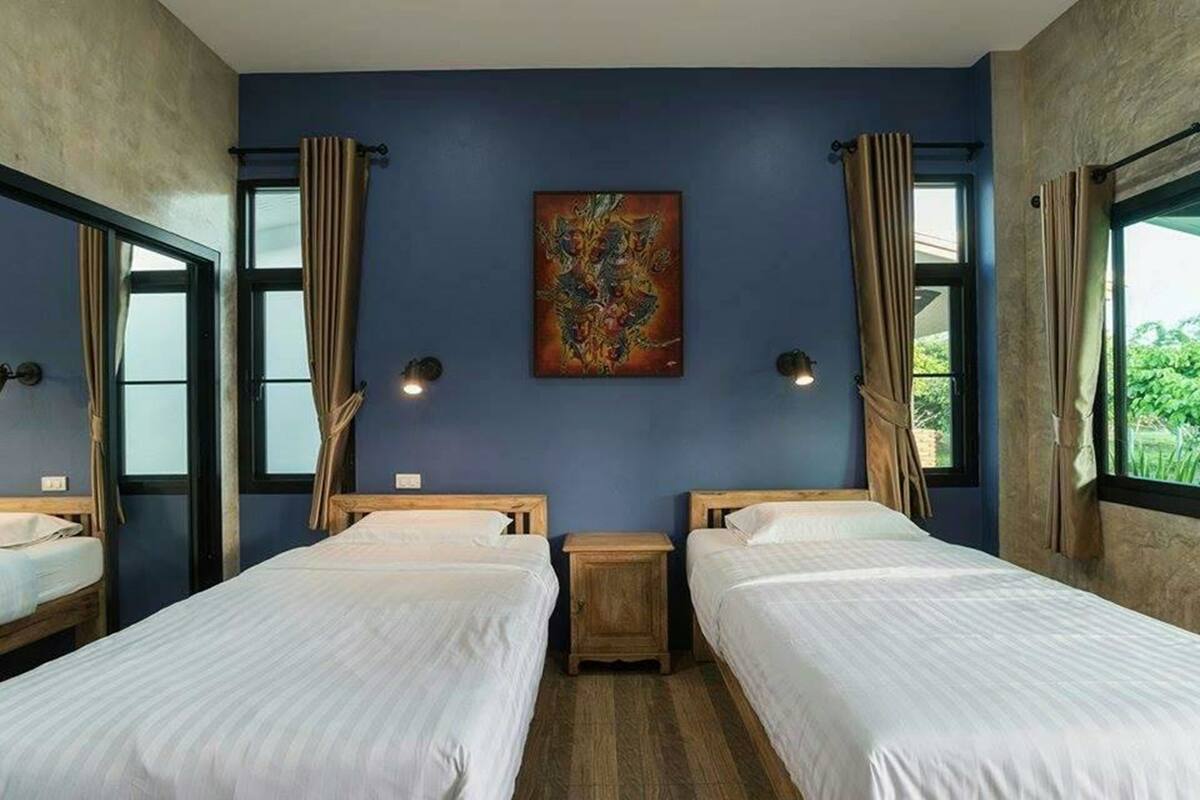 A room with two beds, a painting on the wall, and windows with curtains.