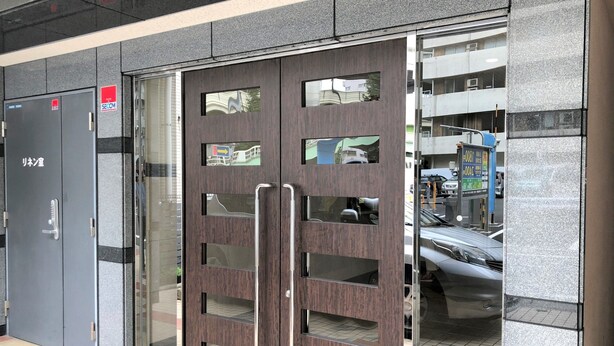 L’entrée d’un hôtel au design moderne, avec une porte en bois foncé dotée de panneaux de verre et de poignées en métal.