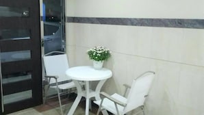 Une petite pièce propre, avec une table et des chaises blanches, une plante en pot et un sol carrelé orné d’un motif géométrique.