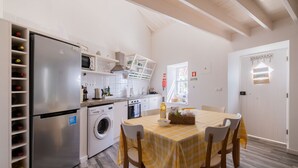 A kitchen with a stainless steel refrigerator, microwave, and oven. There is a dining table with a yellow checkered tablecloth and four chairs. A washing machine is visible in the corner. - Casa Vista da Marquesa, Açores - Ideal house for a couple to enjoy nature! (Nordeste)
