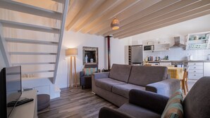 A modern living room with a sofa, armchairs, and a TV. A staircase leads to an upper level. The kitchen is visible with white cabinets and a microwave. - Casa Vista da Marquesa, Açores - Ideal house for a couple to enjoy nature! (Nordeste)