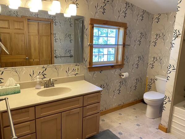 A bathroom with a wooden vanity, a sink, a mirror, a window, and a toilet.