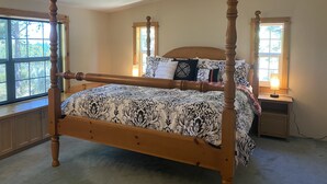 A four-poster bed with a patterned bedspread, two bedside tables with lamps, and a window with a view of trees. - Panoramic view ranch house near Crater Lake (Chiloquin)