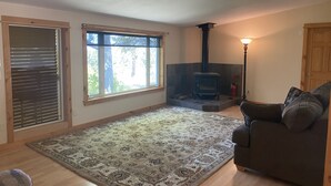 A living room with a fireplace, a sofa, a rug, and a window with blinds. - Panoramic view ranch house near Crater Lake (Chiloquin)