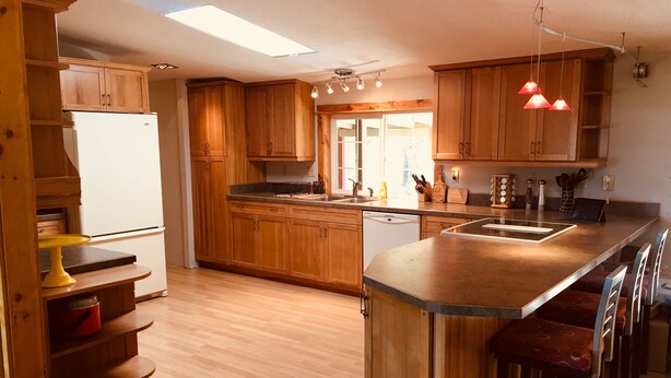 A modern kitchen with wooden cabinets, a central island with bar stools, a built-in dishwasher, and pendant lighting. - Panoramic view ranch house near Crater Lake (Chiloquin)