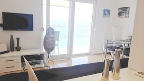 Una sala moderna con televisor, escritorio y una silla cerca de un ventanal corredero que da a un balcón.