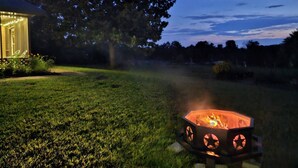 A fire pit in a grassy yard with a house and tree in the background. - Melody's Bed and "Catch Your Breakfast!" (Crockett)