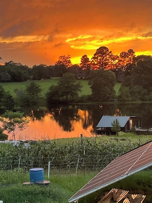 A rural landscape with a sunset, a body of water, and a solar panel.