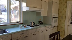 Een keuken met witte kastjes, een fornuis, een spoelbak en een raam met uitzicht op buiten.
