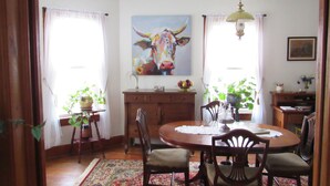Een eetgedeelte met een ronde tafel, stoelen, een vloerkleed en een schilderij van een koe aan de muur.