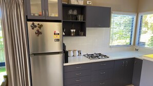 Moderni keittiö, jossa on tummat kaapit, ruostumattomasta teräksestä valmistettu jääkaappi, kaasuliesi ja ikkuna, jossa on sälekaihtimet.