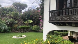 Un jardín con diversas plantas y un edificio blanco con balcón.