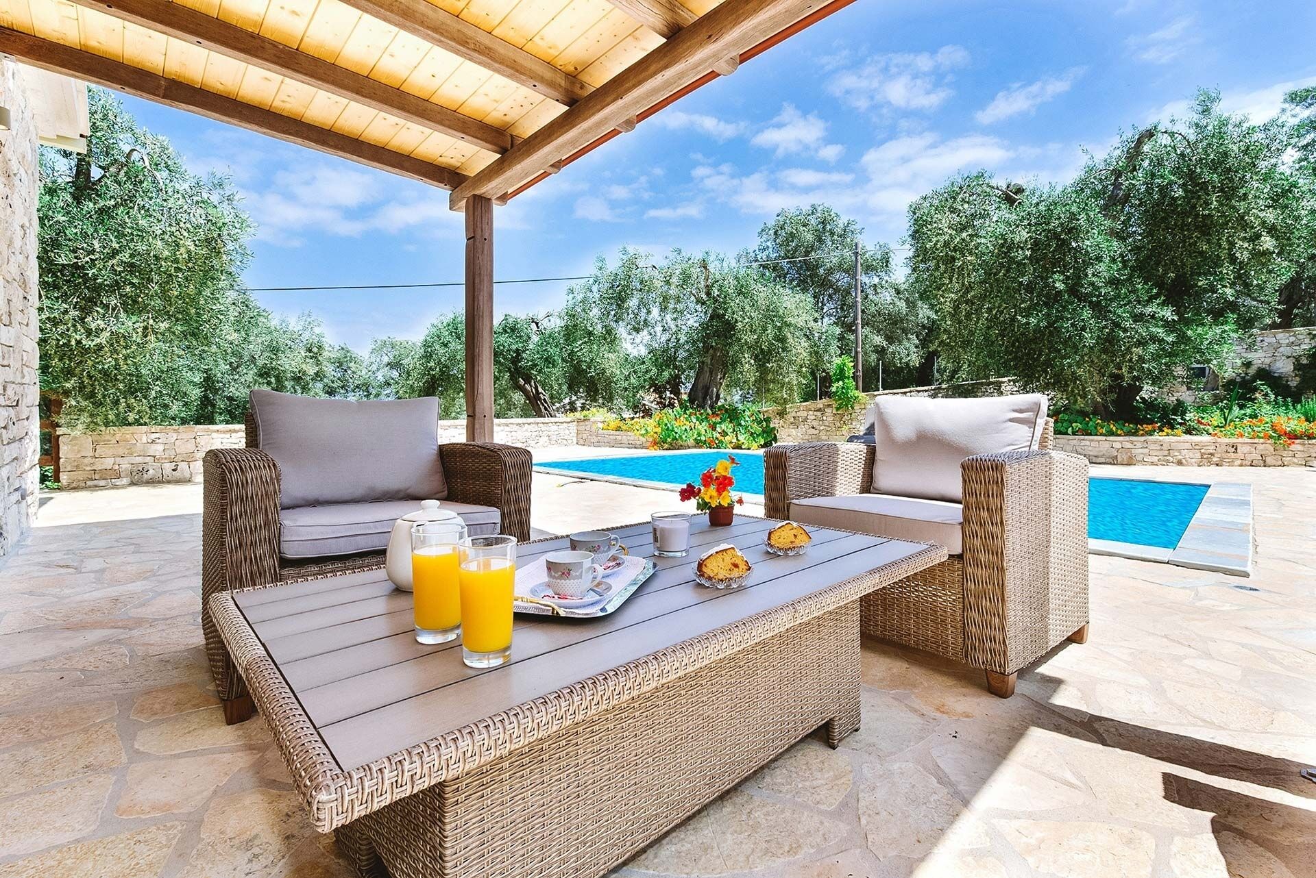Een terras met rieten meubels, een zwembad en een stenen vloer.