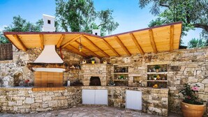 Ein Außenbereich mit Küche, Steinmauern, einer Holz-Pergola und einem Steinboden.