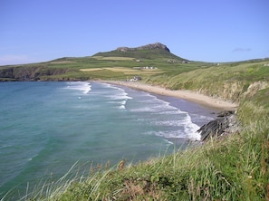 Eine Küstenlandschaft mit Strand, grasbewachsenen Hügeln und einem Berg im Hintergrund.