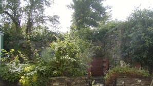 A stone wall with a brick archway leading to a paved area.