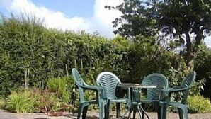 A green plastic table and chairs set outdoors with a hedge and trees in the background.