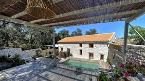Un edificio de piedra con techo de tejas, piscina y terraza de madera.