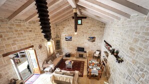 Una habitación rústica con paredes de piedra, techo elevado, sofá, mesa de comedor y televisor.