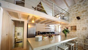 Una cocina moderna con una isla central, paredes de piedra y una zona superior con una escalera.