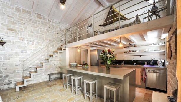 Una cocina moderna con una isla central, taburetes de bar, un refrigerador de acero inoxidable y una pared de piedra.