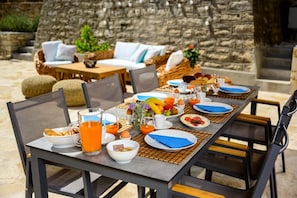 Enjoy a leisurely breakfast in our outdoor dining area, surrounded by lush greenery and a stone wall.