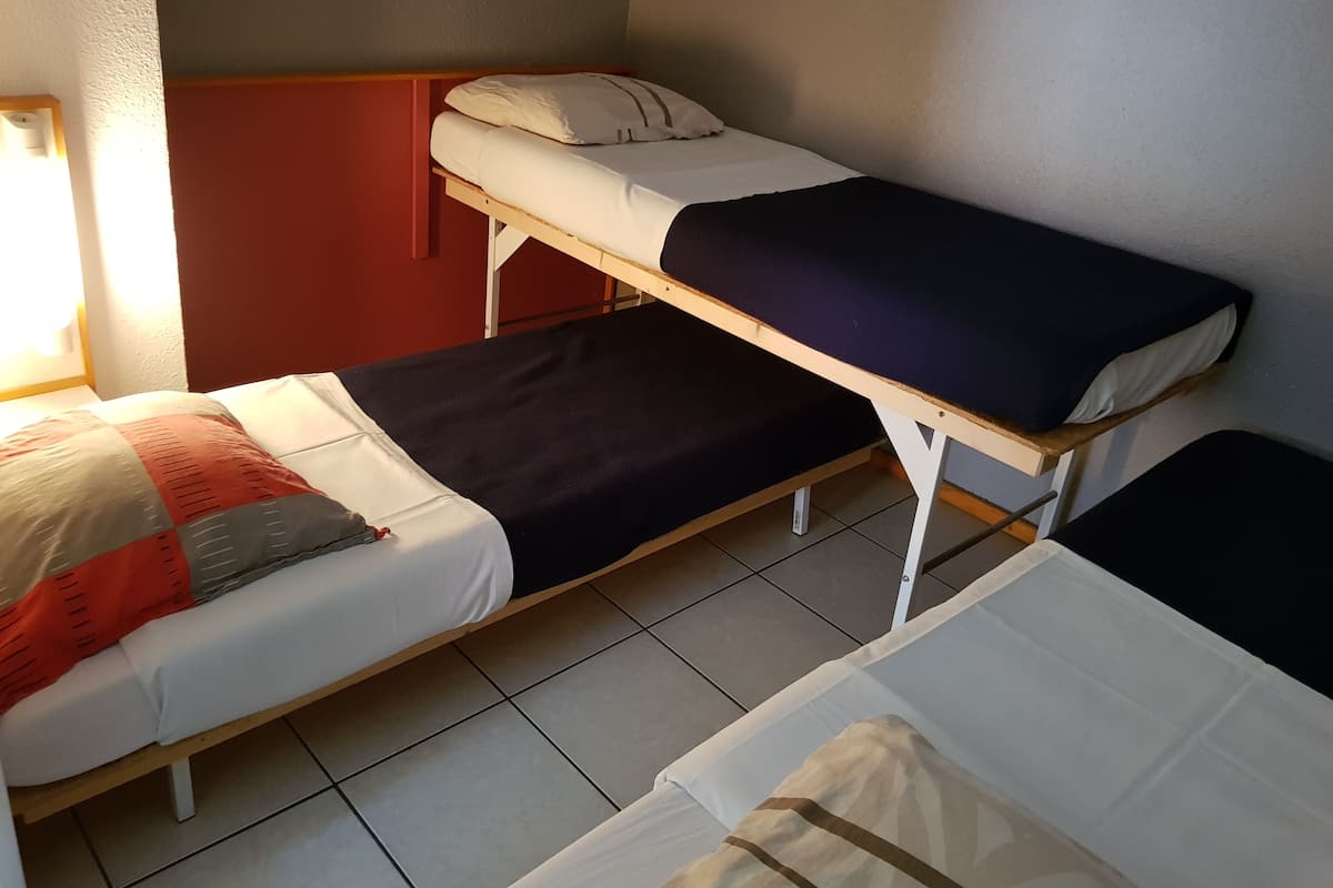 A dormitory room with two bunk beds, each with a pillow and a blanket.