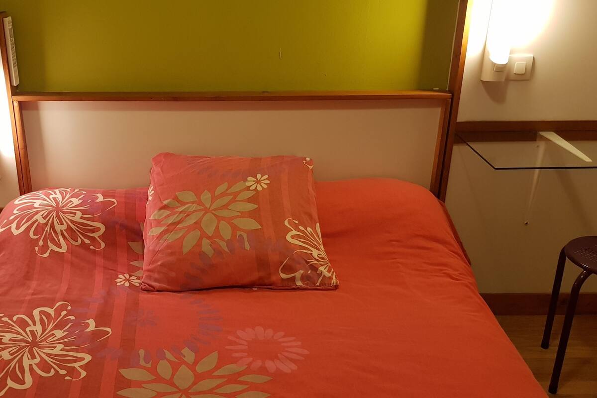 A bed with floral bedding, a nightstand, a chair, and a mirror.
