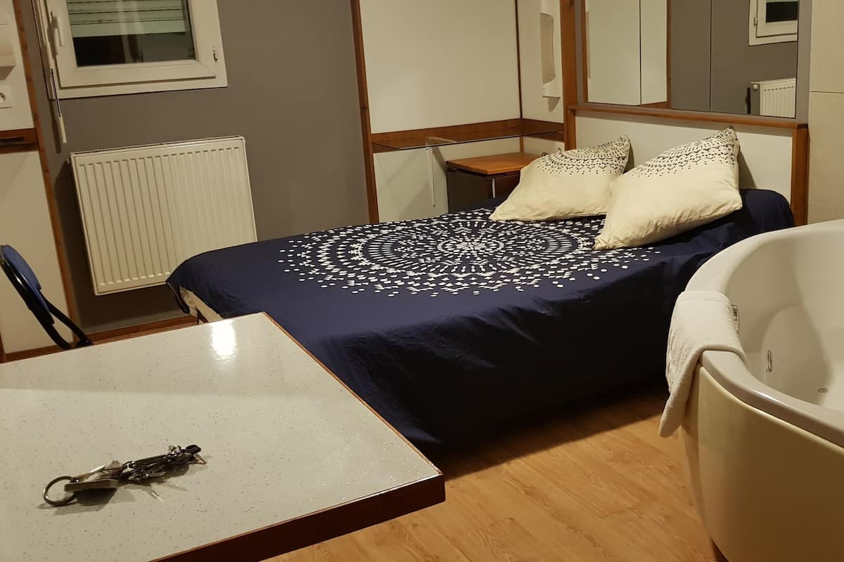 A bedroom with a bed, a small table, a chair, a bathtub, and a radiator.