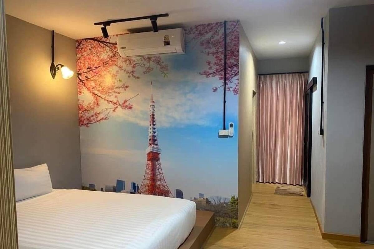 A hotel room with a bed, a wall mural of the Eiffel Tower, a ceiling fan, and a window with curtains.