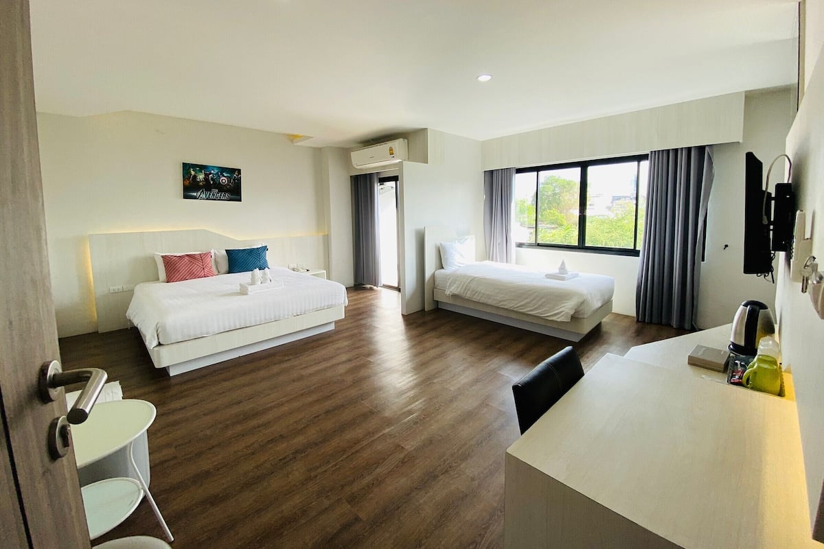 A hotel room with two beds, a desk, a chair, an air conditioning unit, and a window with curtains.