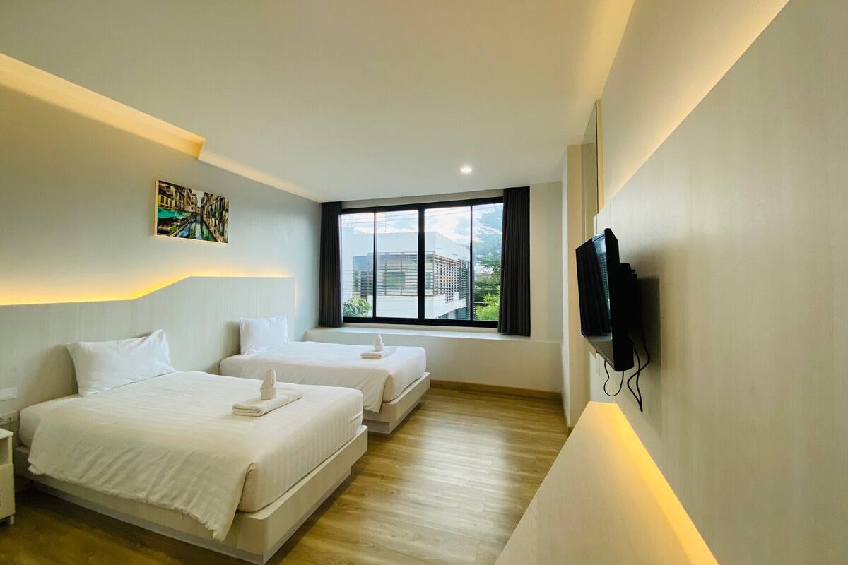 A hotel room with two beds, a TV, a painting, and a window with a city view.