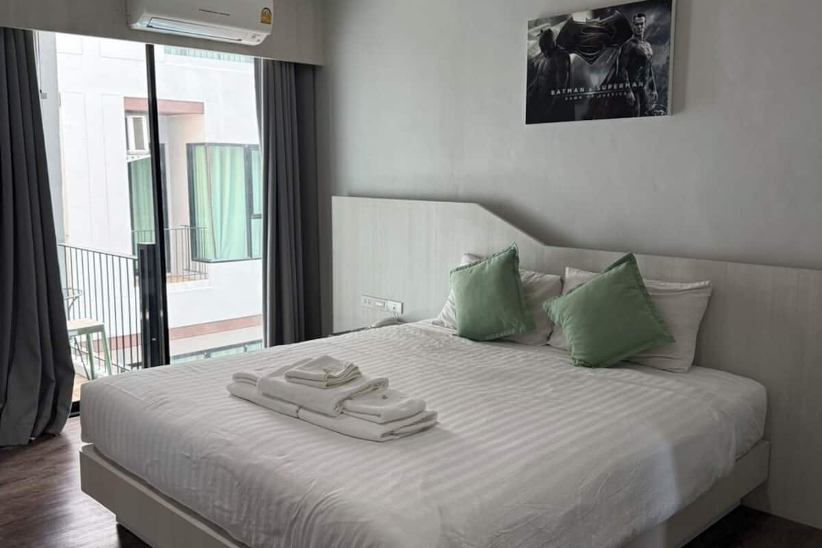 A hotel room with a large bed, a view of the outside, and a Batman & Superman poster on the wall.