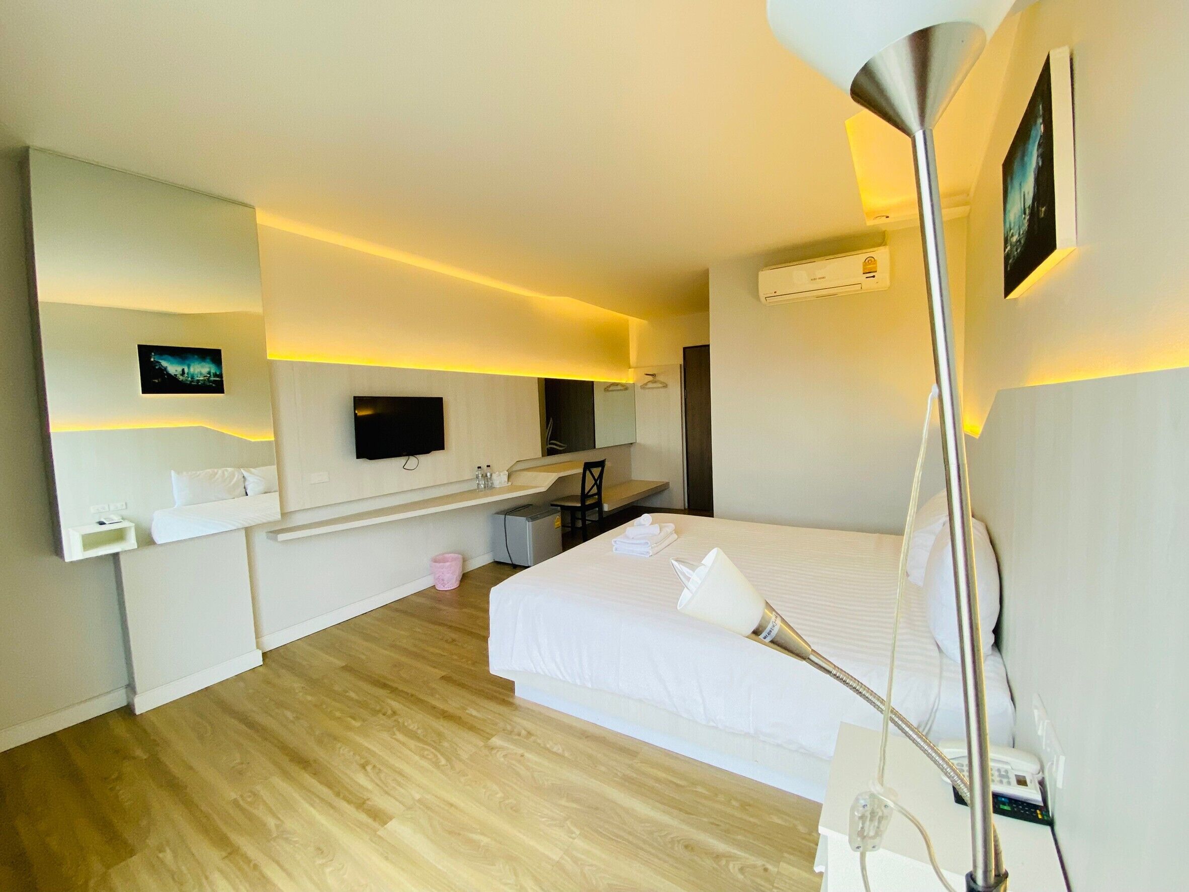 A modern hotel room with a large bed, a flat-screen TV mounted on the wall, a bedside table with a lamp, and a small desk with a chair.